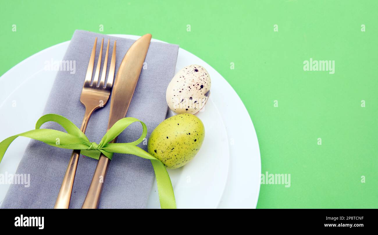 Impostazione tavolo di Pasqua, decorazione uova di Pasqua, tovagliolo e posate dorate su piatti bianchi, sfondo verde pastello Foto Stock