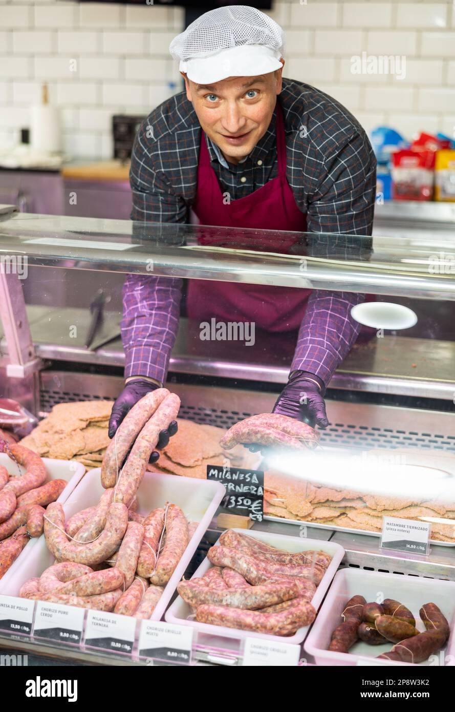 Macellaio maschio positivo con salsiccia di manzo fresca in macelleria Foto Stock