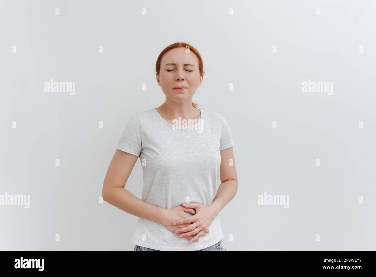 Una giovane donna tiene lo stomaco nel dolore. Problemi digestivi, concetto di malattie gastrointestinali. Fondo bianco. Foto Stock