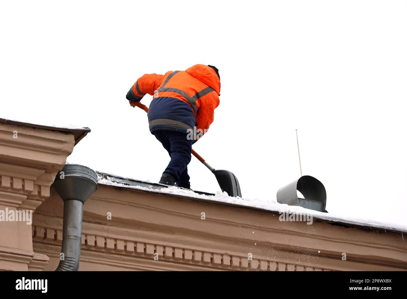Lavoratore che rimuove la neve sul tetto di un edificio. Rimozione della neve, pulizia del tetto in inverno o all'inizio della primavera Foto Stock