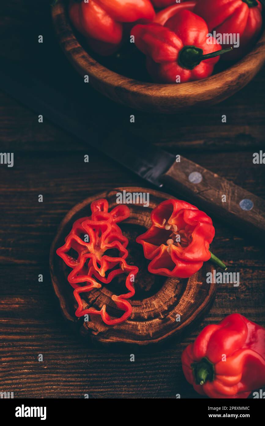 Peperoni Habanero Chili rossi e uno affettato su una superficie di legno scuro Foto Stock