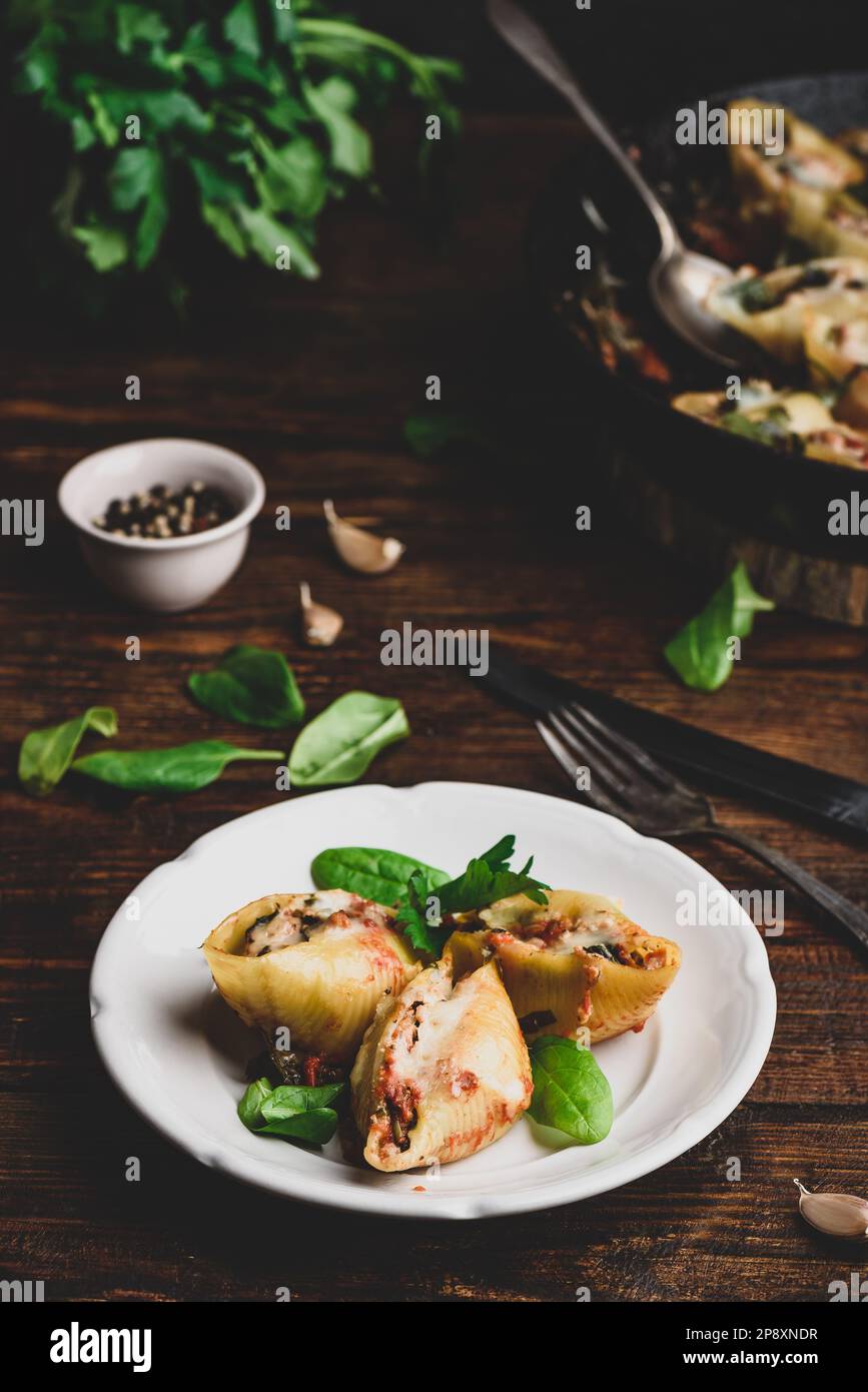 Conchiglie al forno farcite con manzo macinato, spinaci e formaggio su piatto bianco Foto Stock