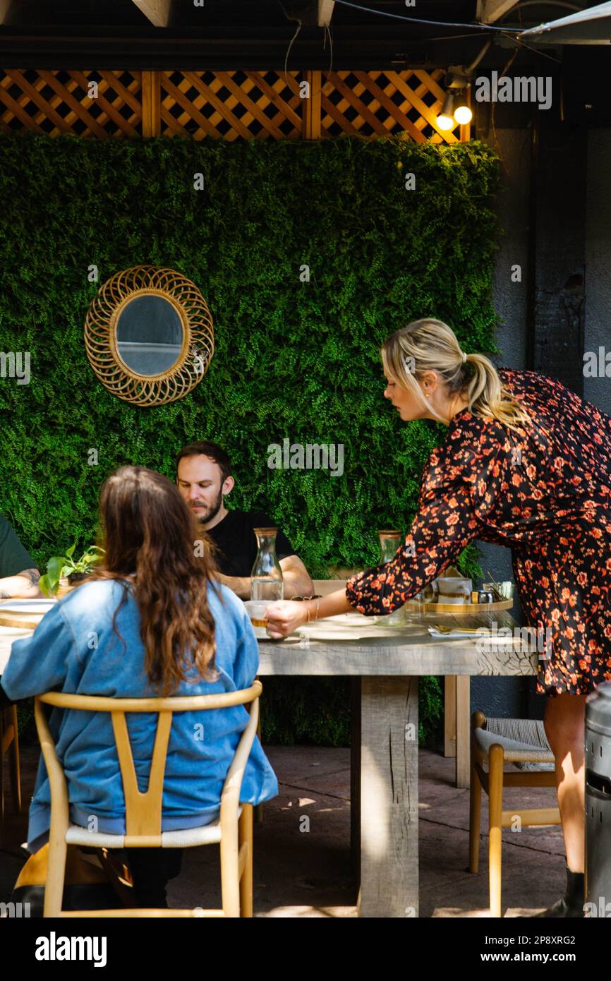 Un server offre piatti a un tavolo in una sala da pranzo all'aperto con un ambiente naturale Foto Stock