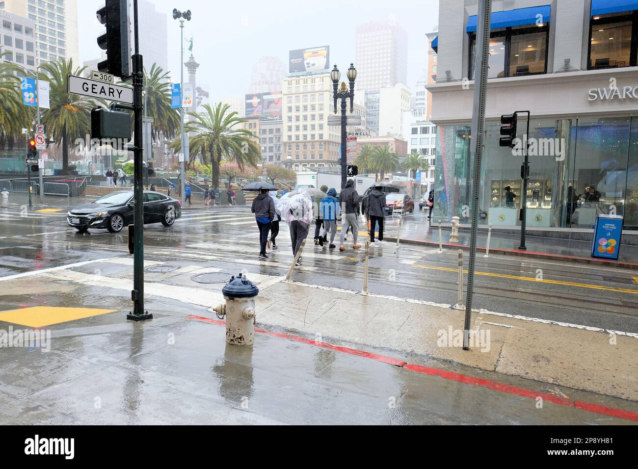 Pedoni e turisti sotto la pioggia nel centro di San Francisco, California; persone in condizioni di pioggia e tempo umido in visita sul marciapiede e strada Foto Stock