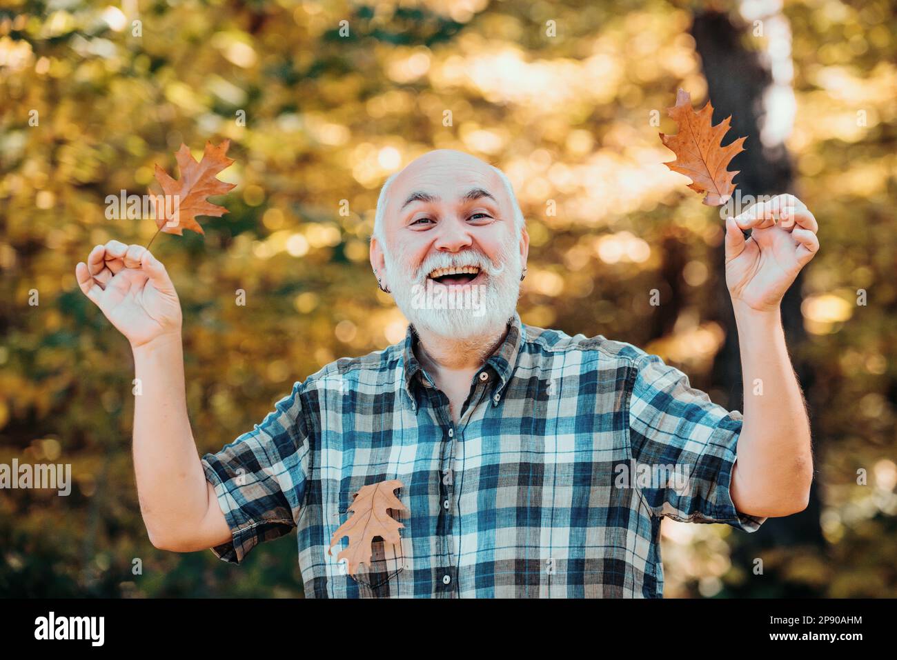 Uomo anziano sorridente all'aperto nella natura. Nonno relax nel parco autunnale. Concetto di pensionamento libero. Uomo anziano che cammina nel parco in autunno. Foto Stock