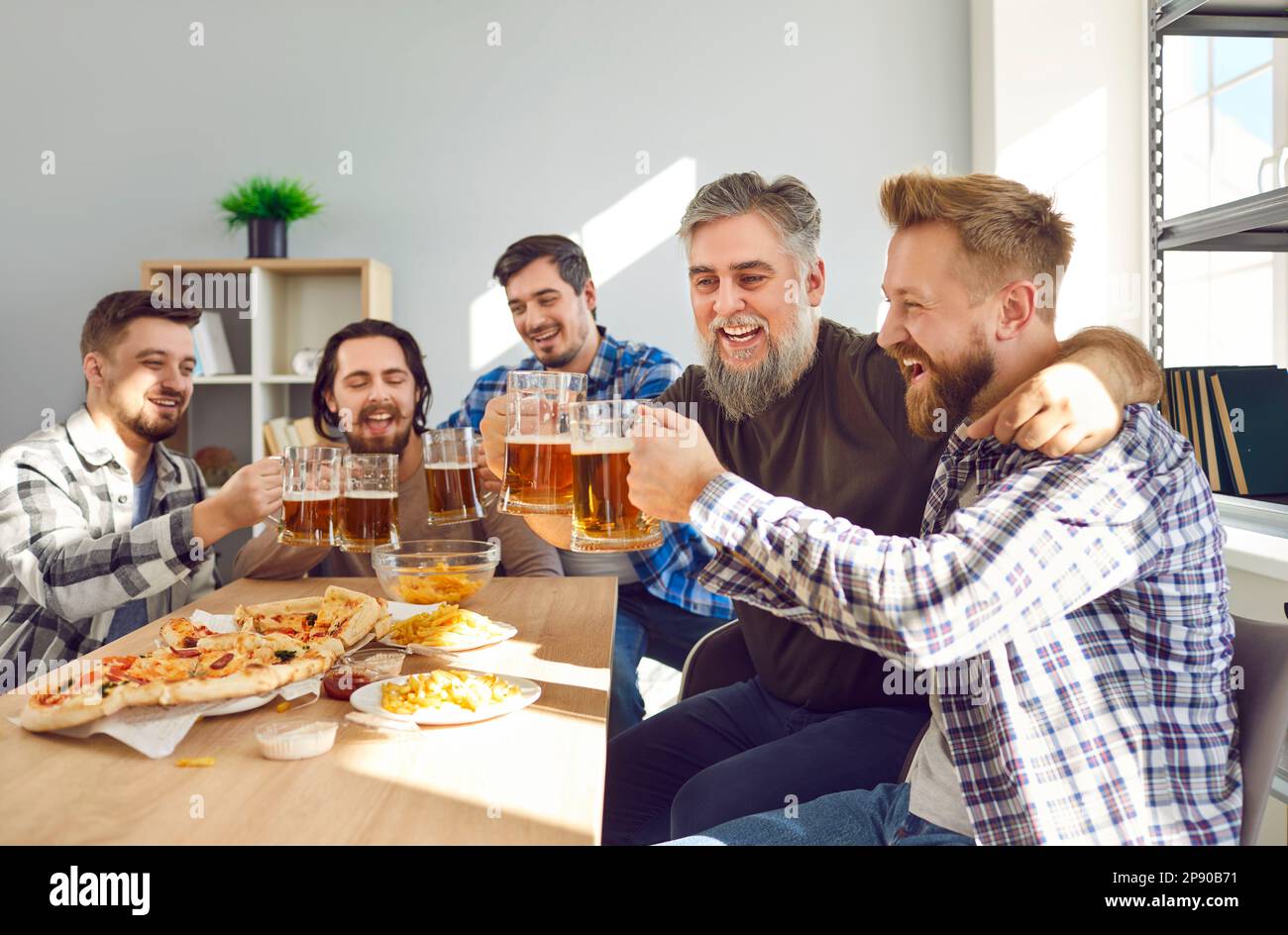 Amici maschi sorridenti con birra e pizza che si divertono seduti a casa. Foto Stock