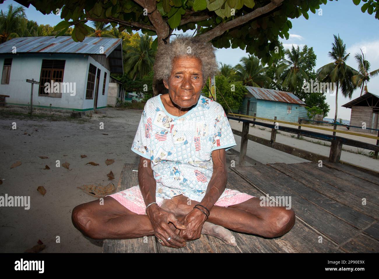 Vecchia donna seduta a gambe incrociate sotto l'albero, villaggio di Saporkren, provincia di Waigeo, Raja Ampat, Papua Occidentale, Indonesia Foto Stock