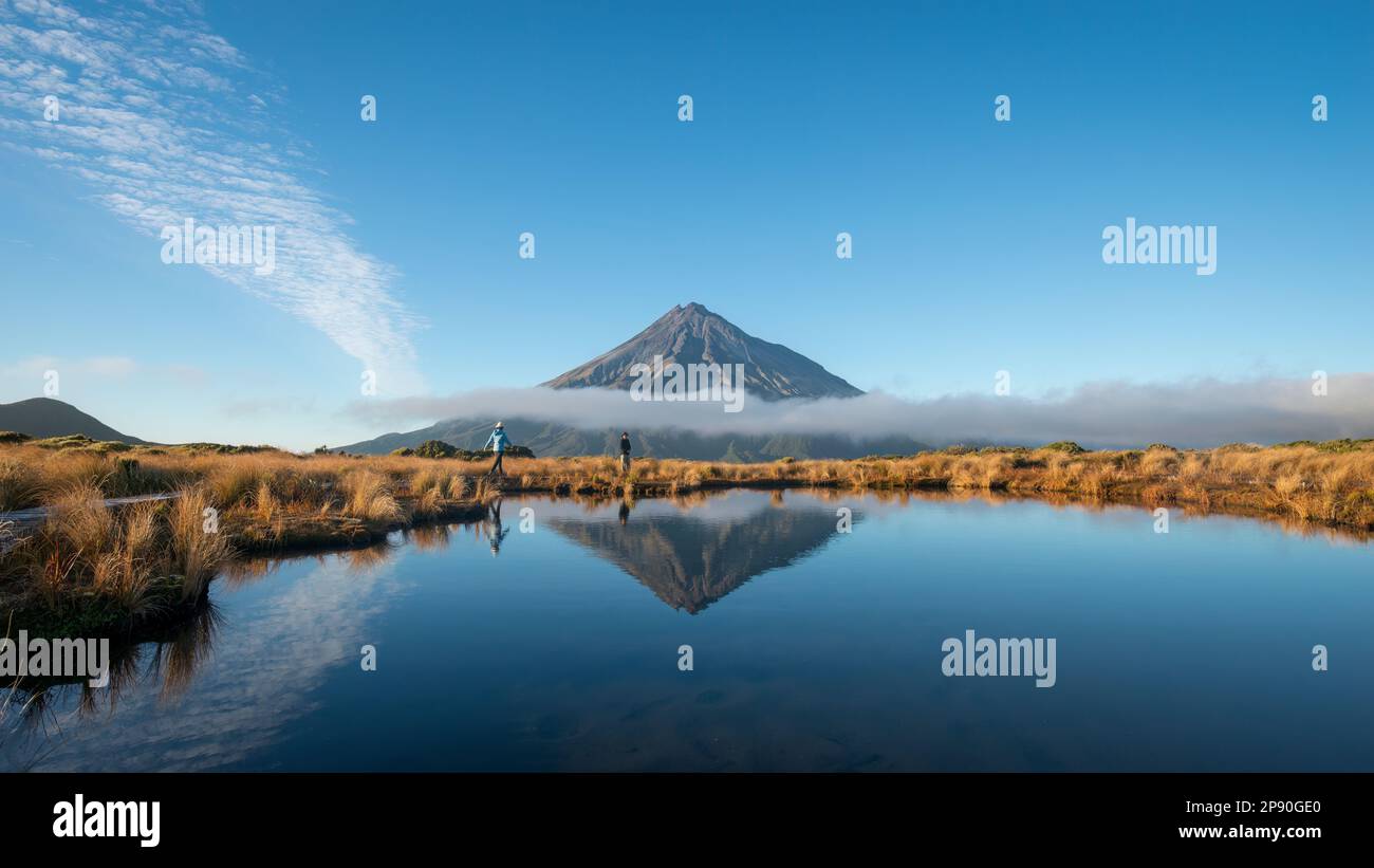 Coppia trekking Pouakai circuito. Il Monte Taranaki si riflette nel tarn Pouakai. Nuova Zelanda. Foto Stock