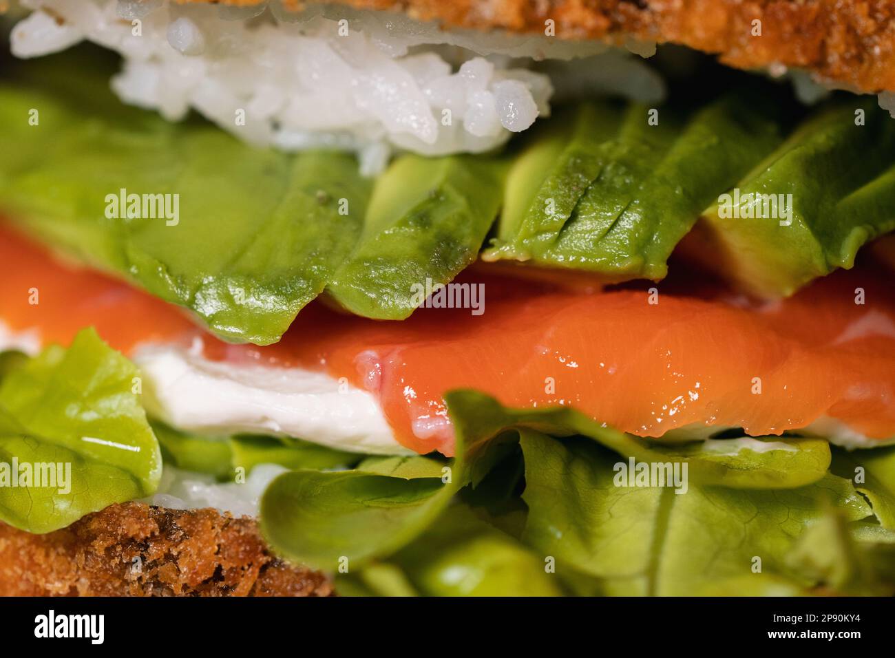 Primo piano di un panino di salmone crudo appena preparato con avocado, formaggio cremoso, riso fritto e lattuga Foto Stock