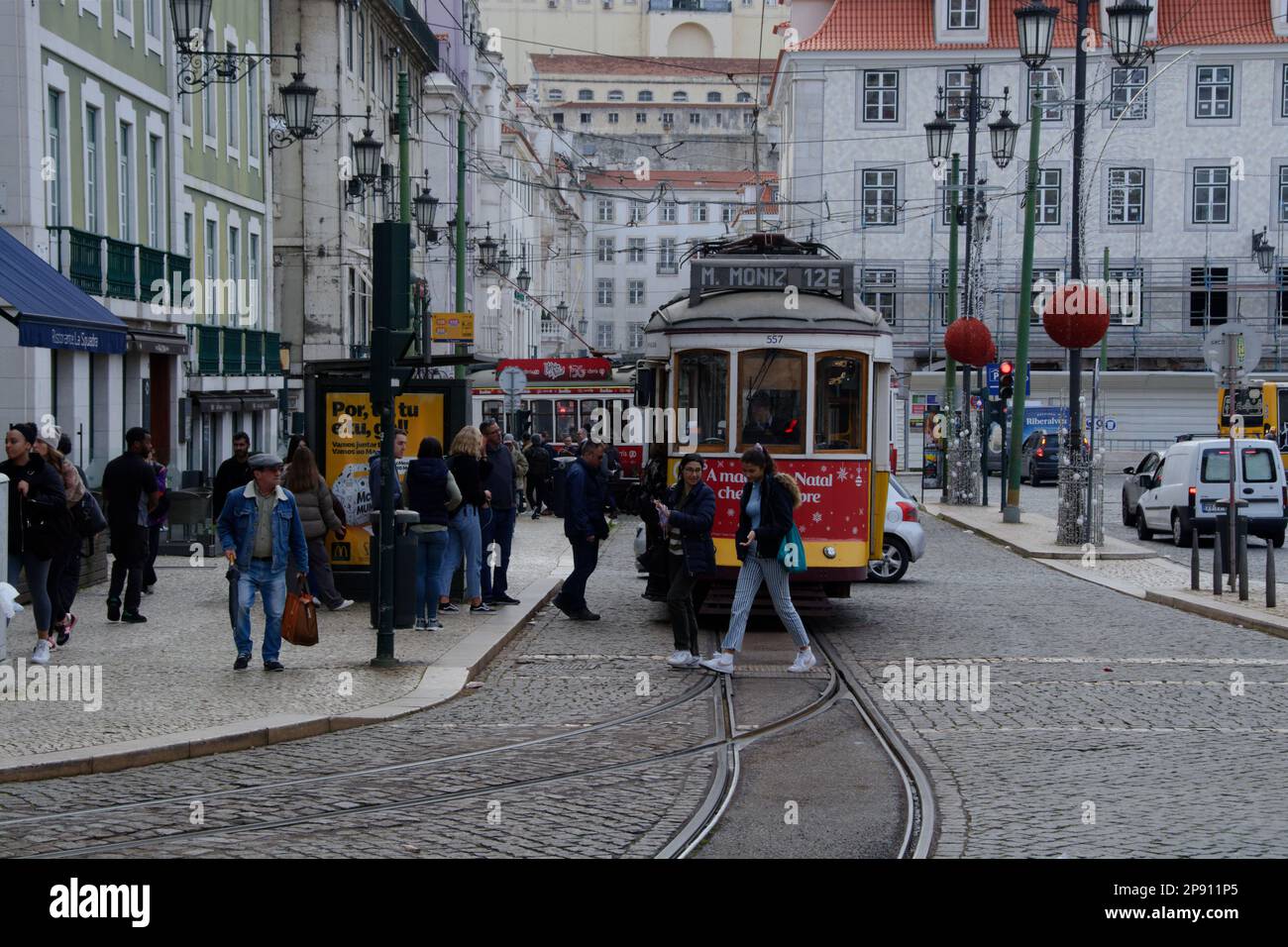 Lisbona Tram alla fermata del tram con pedoni e secondo tram in background. Vista frontale del tram 12E in attesa di partenza. Sfondo dell'edificio cittadino. Foto Stock