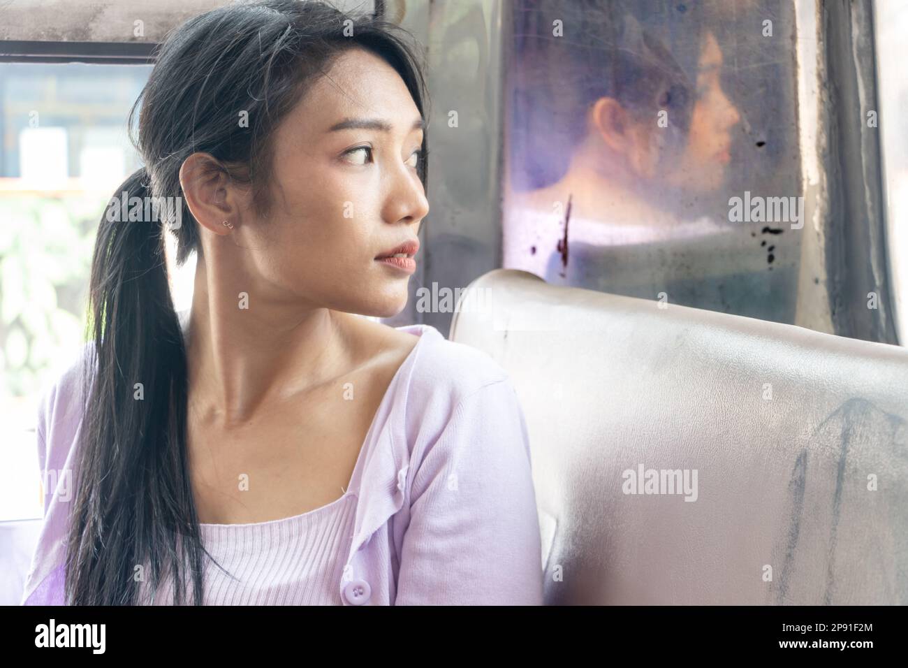 Una giovane donna siede su un vecchio autobus e guarda indietro attraverso il finestrino posteriore Foto Stock