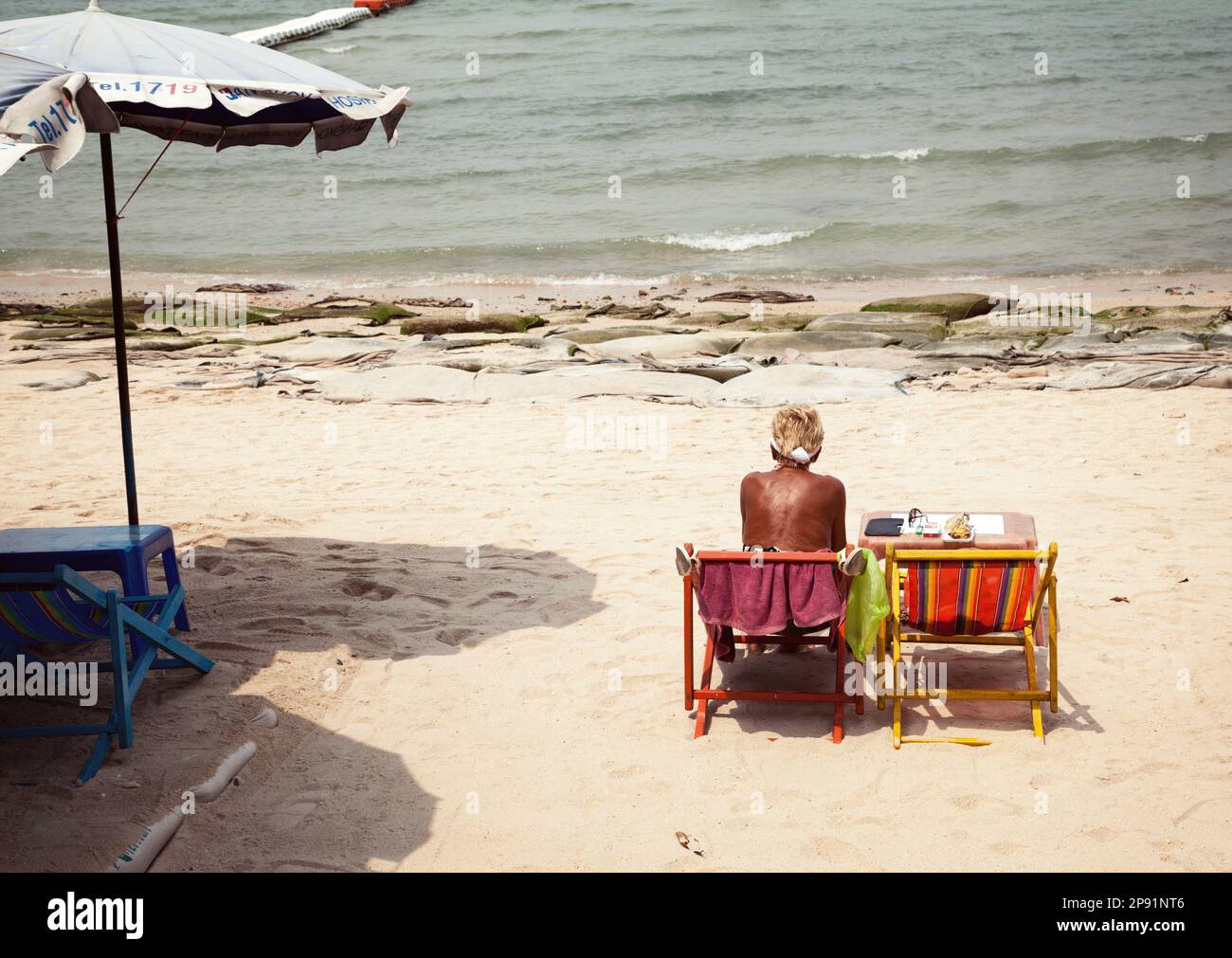 Pattaya, Thailandia - 24 marzo 2016: Donna anziana, solitaria, triste alla spiaggia sporca, caotica e soleggiata. Sfortunato, cattivo, noioso viaggio di vacanza al mare Foto Stock