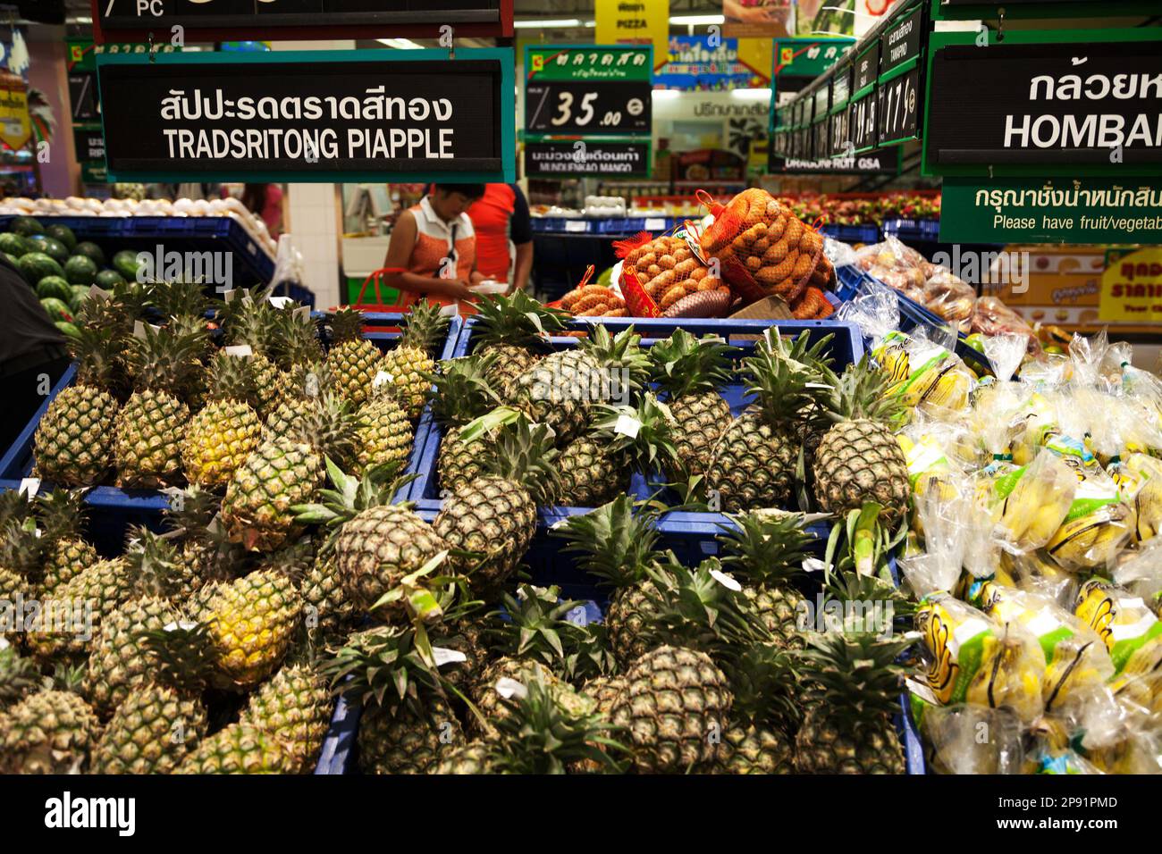 Pattaya, Thailandia - 23 marzo 2016: Scaffale asiatico supermercato: Mucchio di ananas, banane e altri frutti. Cartello di mercato tailandese e inglese: Ortografia sbagliata Foto Stock