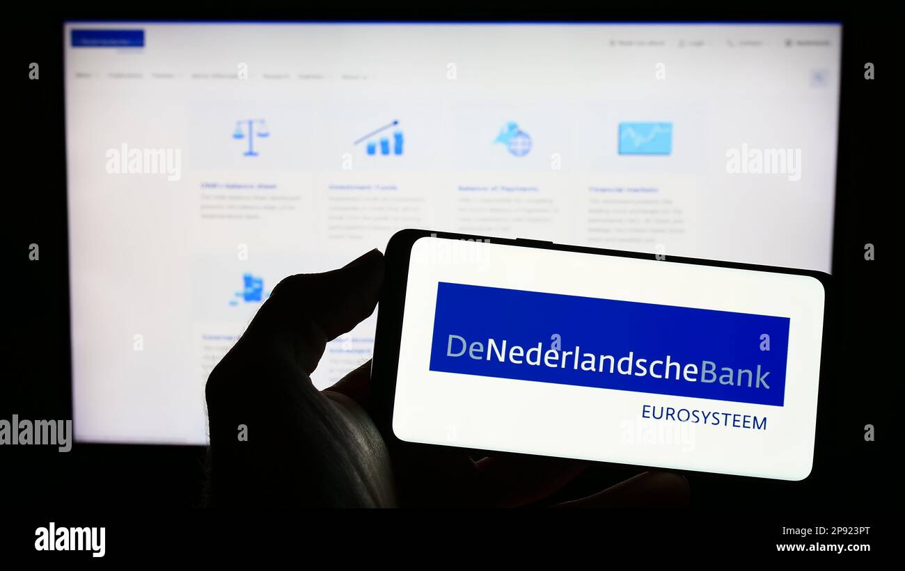 Persona che tiene il cellulare con il logo della banca centrale olandese De Nederlandsche Bank (DNB) sullo schermo di fronte alla pagina web. Messa a fuoco sul display del telefono. Foto Stock