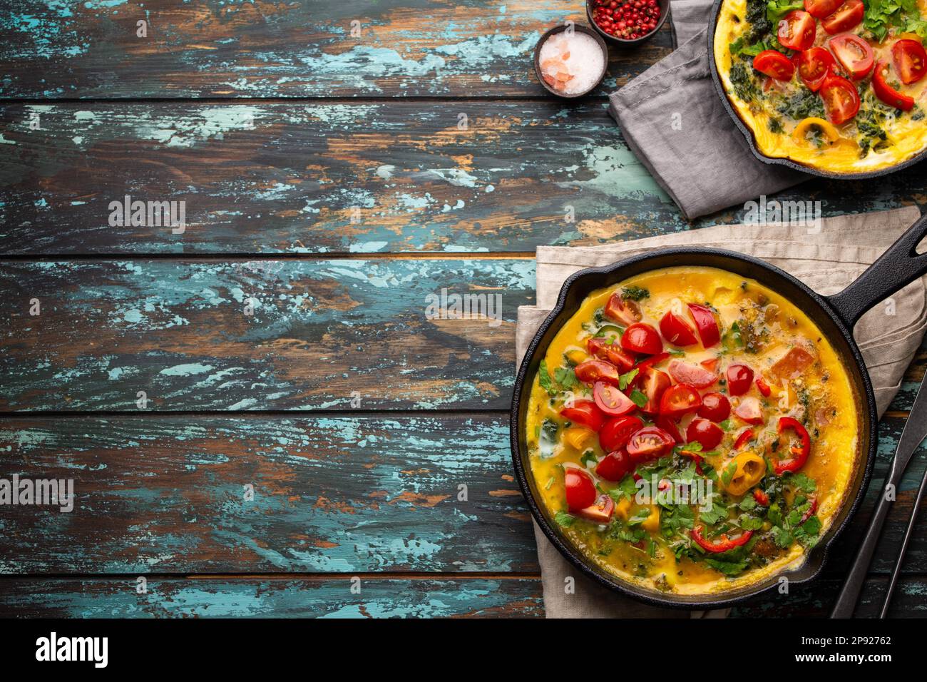 Frittata sana in due padelle di ghisa con uova sbattute fritte e verdure di stagione su sfondo rustico in legno. Omelette italiana con biologico Foto Stock