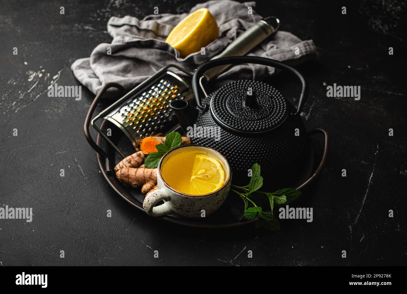 Tè curcuma di erbe caldo sano per amplificare il sistema immunitario. Ingredienti per preparare tè disintossicante in tazza, teiera nera, radice di curcuma fresca, limone, menta Foto Stock