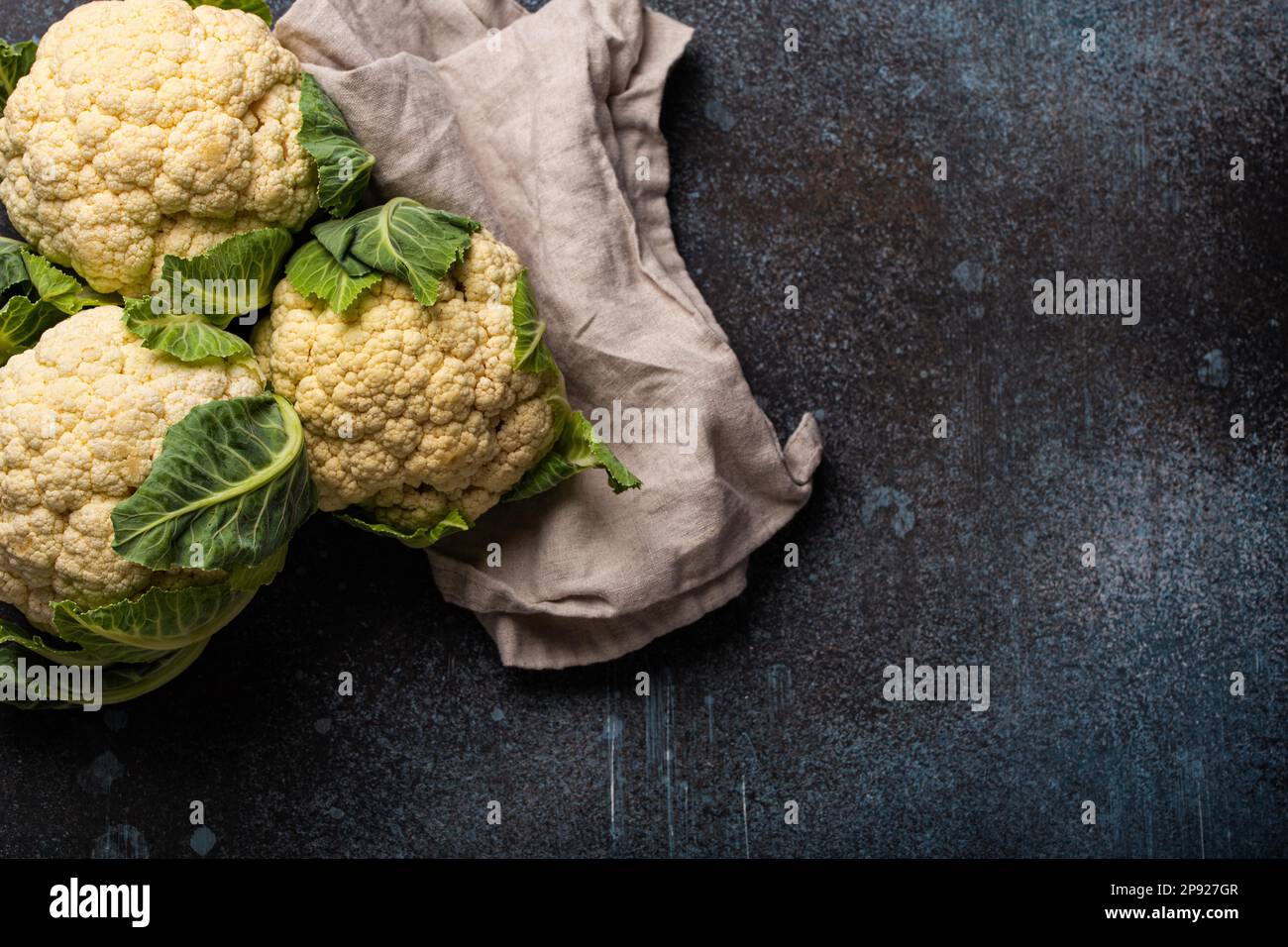 Cavolfiore bianco fresco intero organico su tavola di fondo vintage pietra scura, pronto per essere cucinato, vista dall'alto con spazio copia. Cibo vegetariano, pulito Foto Stock