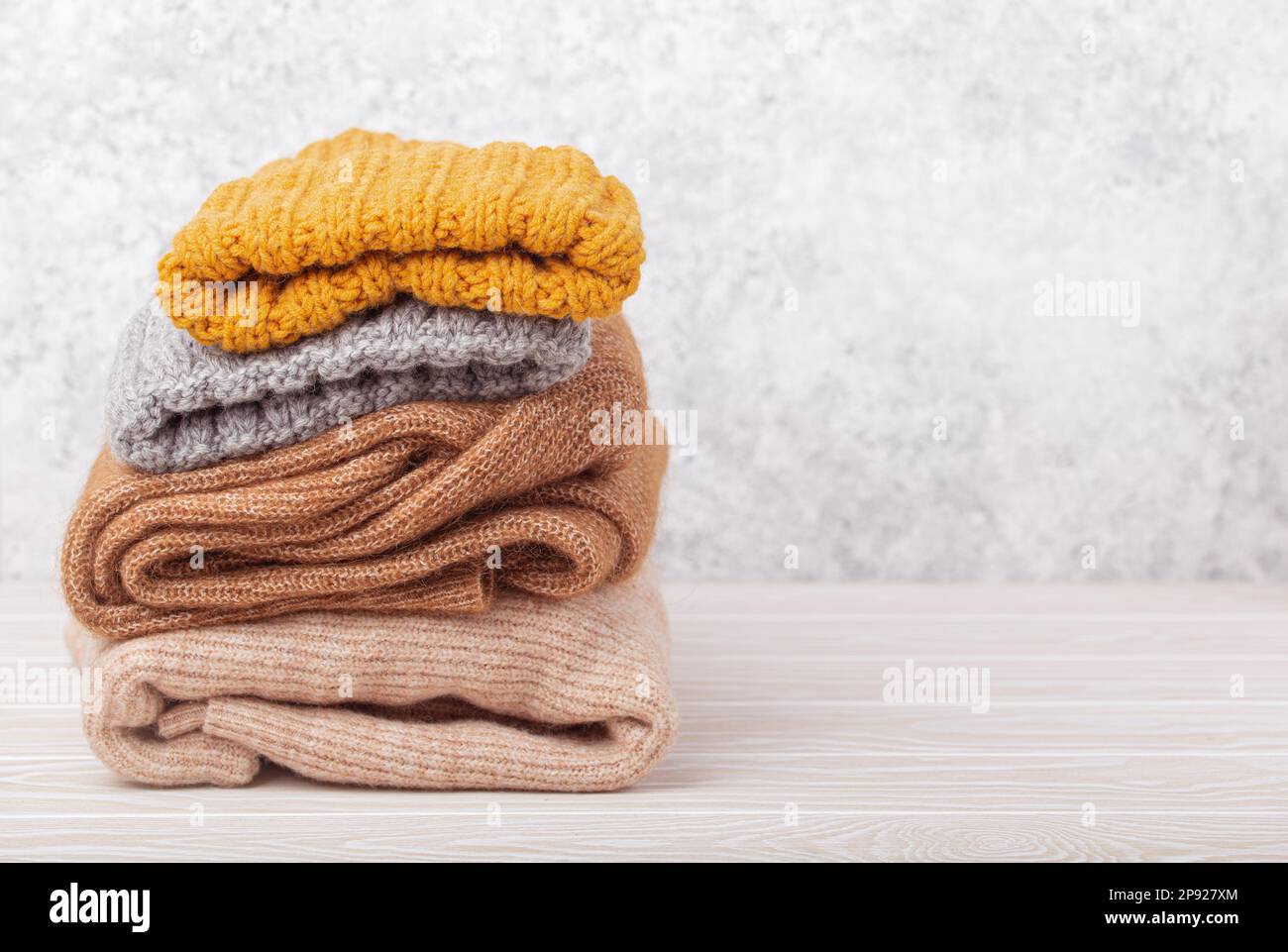 Pile di abiti caldi a maglia, maglioni e berretti su sfondo rustico in legno bianco. Intimo pile a maglia ripiegato, guardaroba invernale a capsula Foto Stock