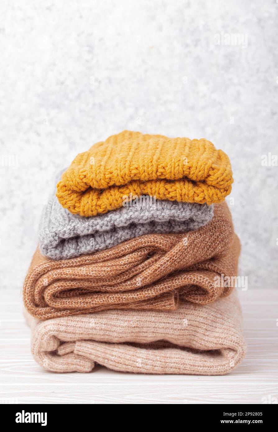 Pile di abiti caldi a maglia, maglioni e berretti su sfondo rustico in legno bianco. Intimo pile a maglia ripiegato, guardaroba invernale a capsula Foto Stock