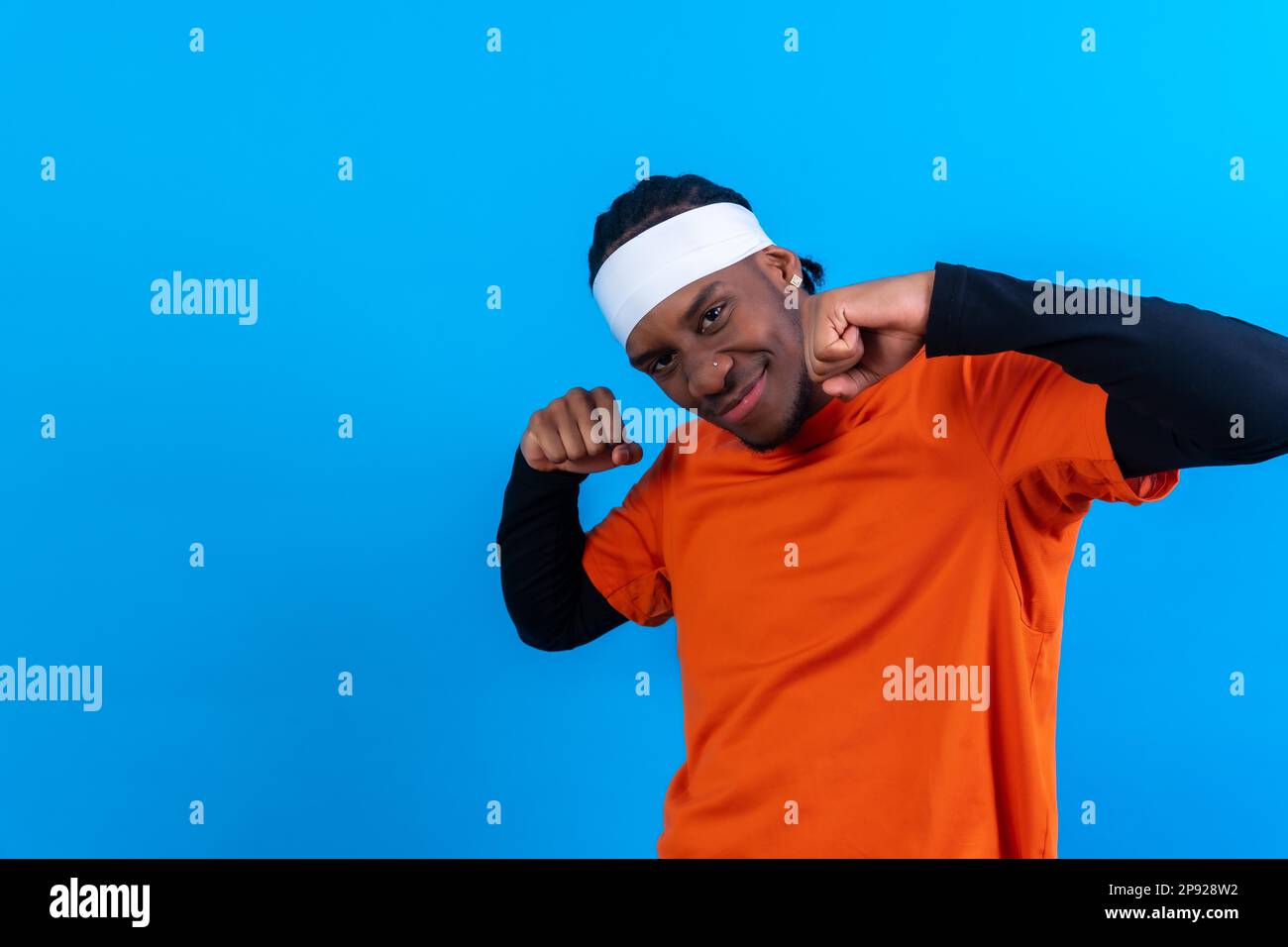 Uomo etnico nero in abiti arancioni su sfondo blu, sorridente e ballando bene Foto Stock