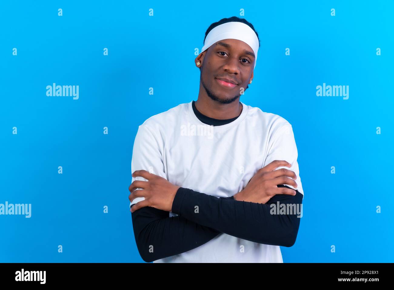 Uomo etnico nero in abiti bianchi su sfondo blu, braccia incrociate Foto Stock