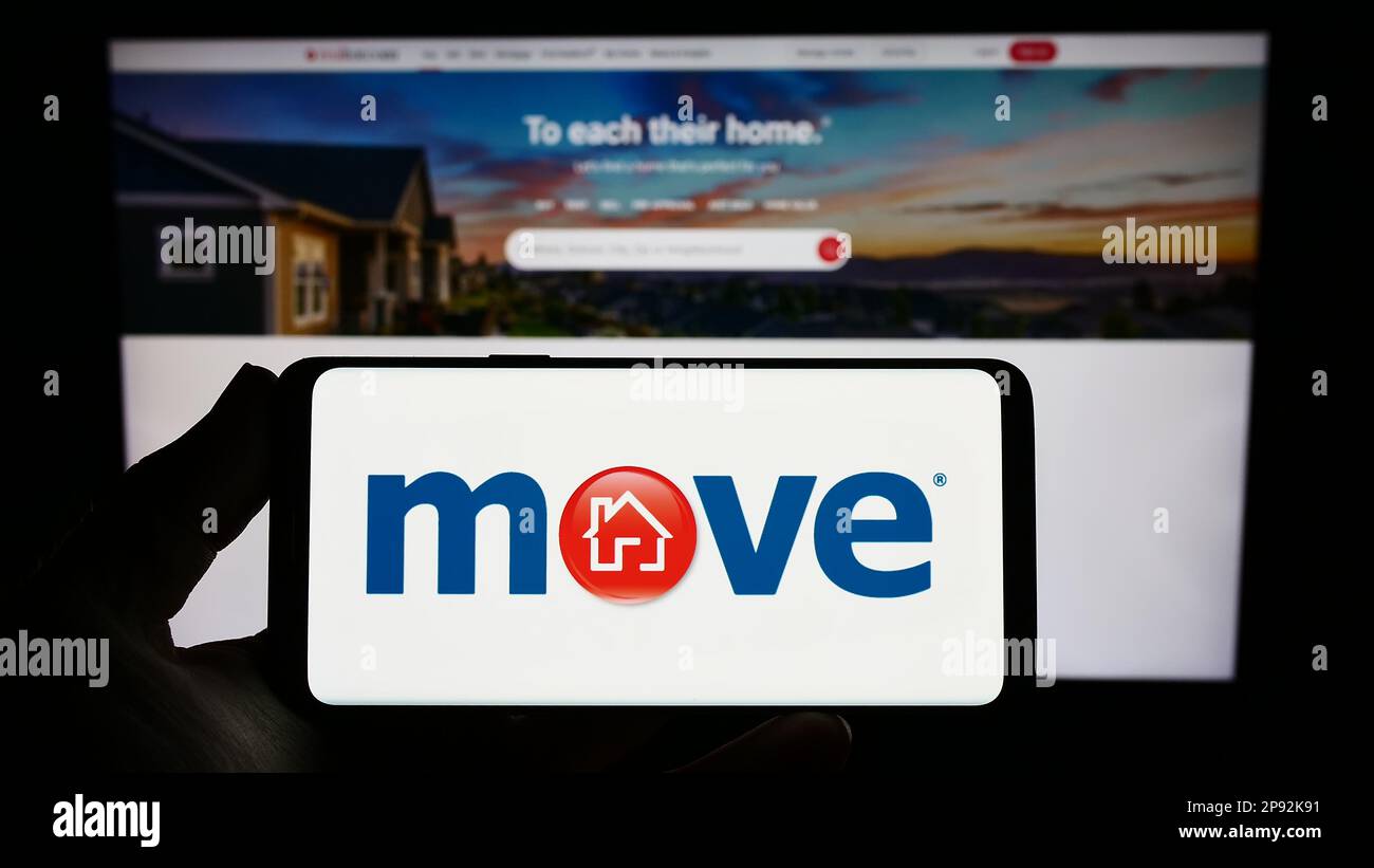 Persona in possesso di smartphone con il logo della società immobiliare statunitense Move Inc. Sullo schermo di fronte al sito Web. Messa a fuoco sul display del telefono. Foto Stock