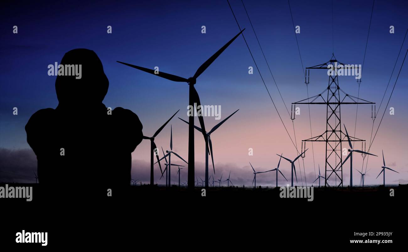 Persona con giacca con cappuccio davanti alle turbine eoliche e alle linee elettriche Foto Stock