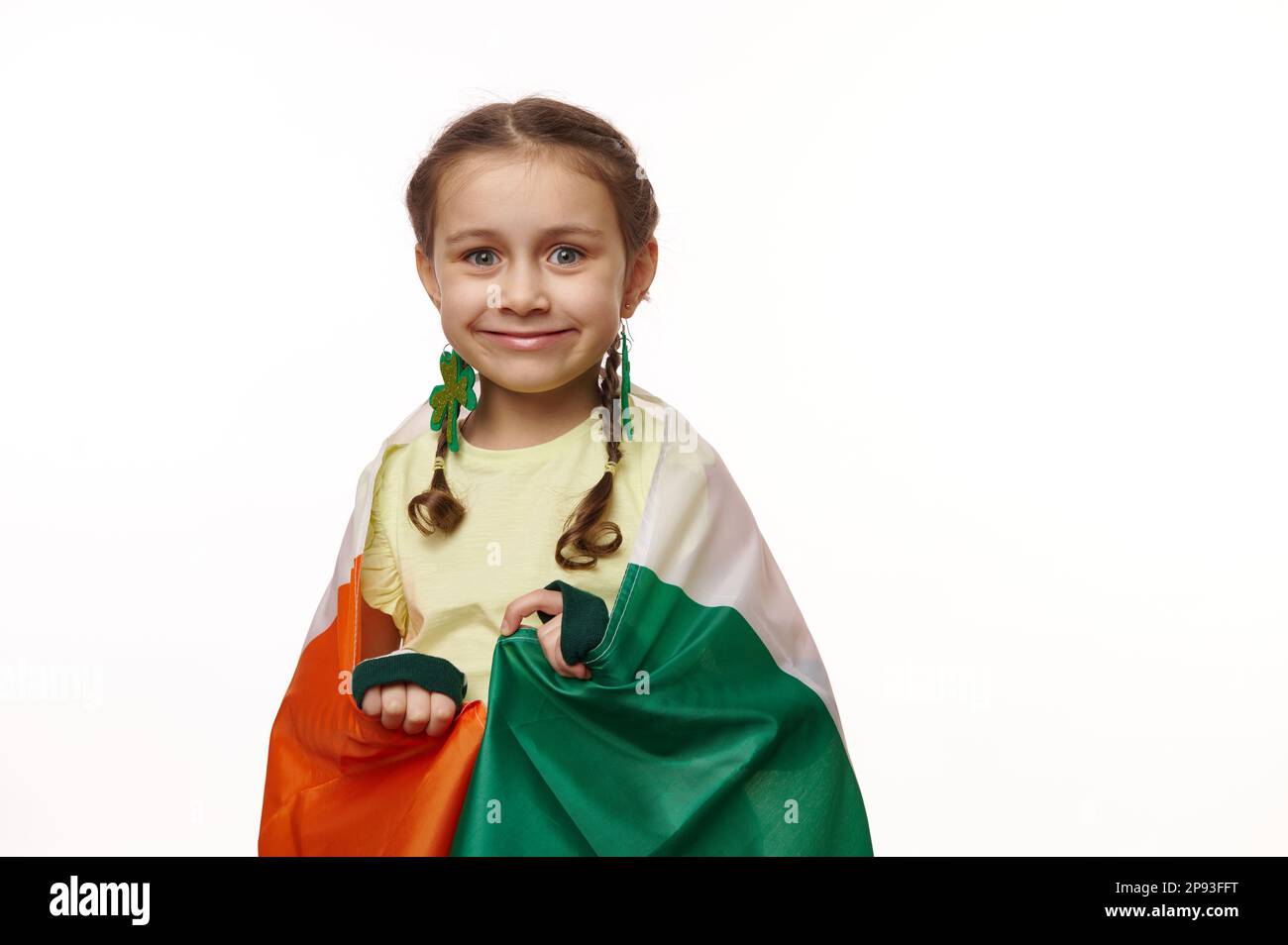 Bella bambina con spirali divertenti, in posa avvolto in bandiera irlandese su sfondo bianco isolato. San Patrizio Foto Stock