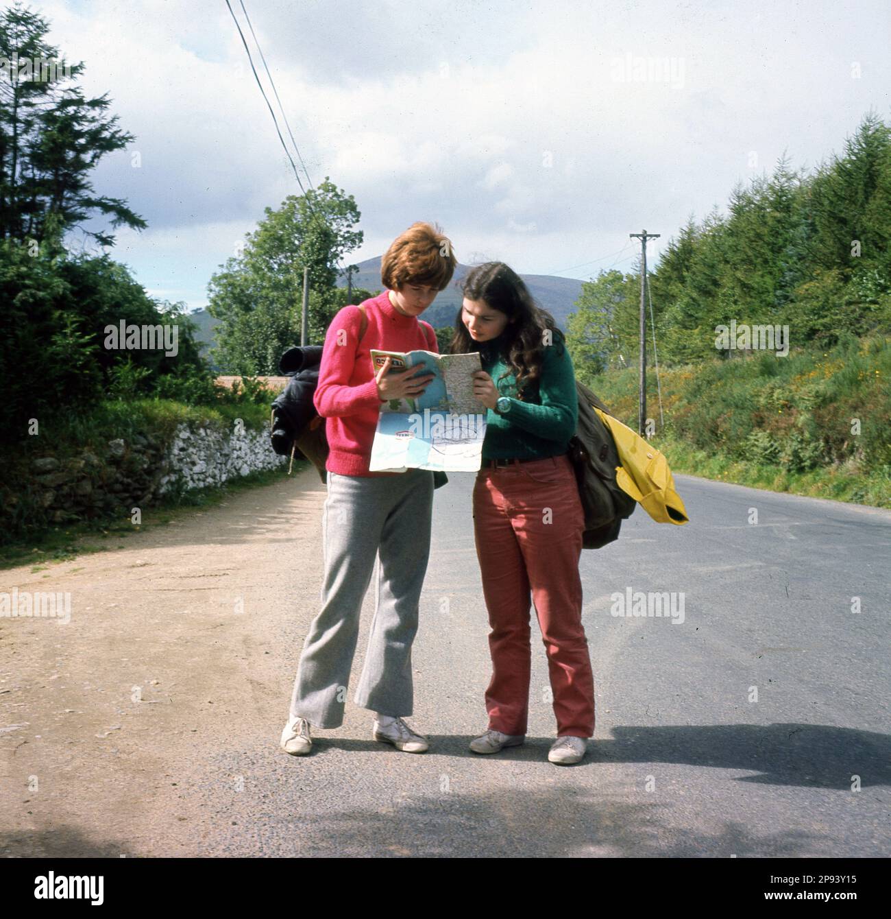 1970s, storico, due giovani donne, 18-20 anni, escursioni sulle montagne di Wicklow, Irlanda, in piedi accanto a una strada, studiando una mappa. Foto Stock