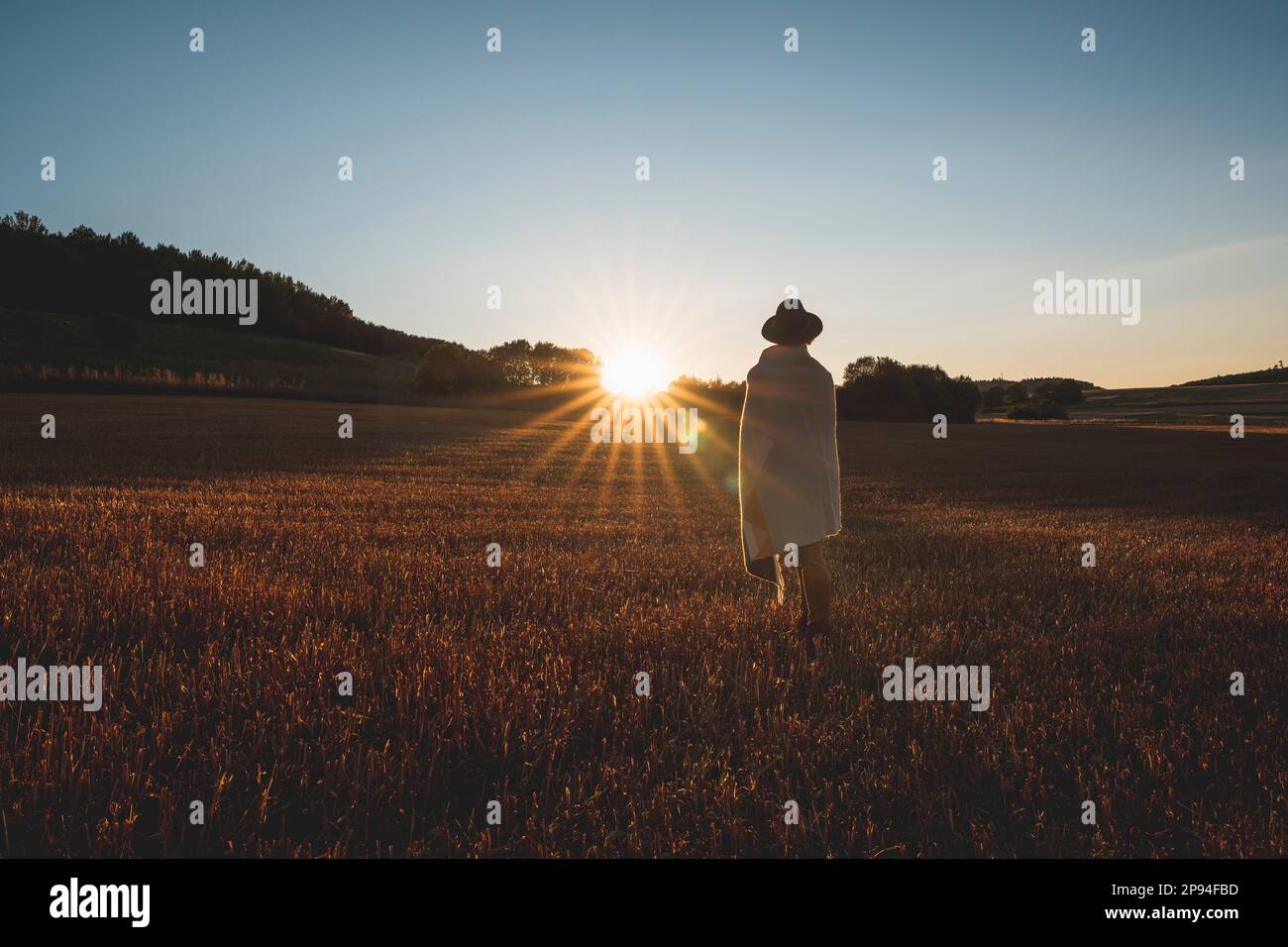 Donna con cappello e coperta di lana in campo stoppia, tramonto Foto Stock