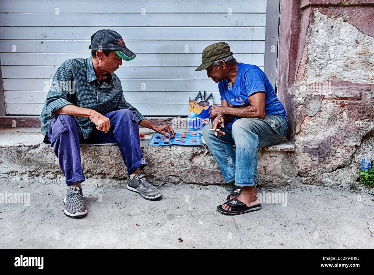 L'AVANA, CUBA - 1 GENNAIO 2020: Due uomini non identificati giocano un gioco di dama sui marciapiedi dell'Avana che si siedono su un gradino della porta. Foto Stock
