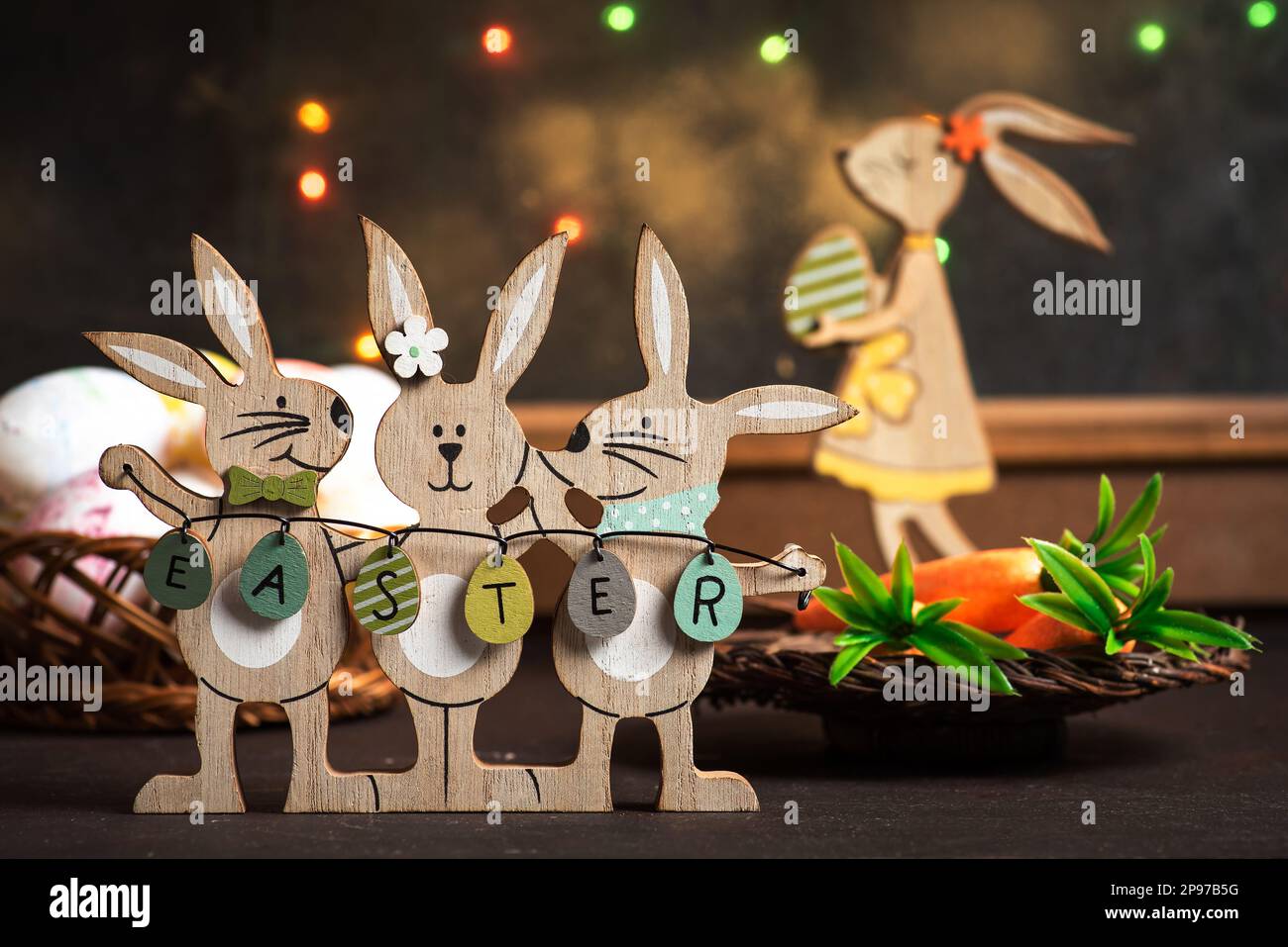 Tre coniglietti pasquali in legno che tengono uova di Pasqua esposti come decorazioni su un tavolo di legno di fronte ad una finestra con decorazioni festive Foto Stock