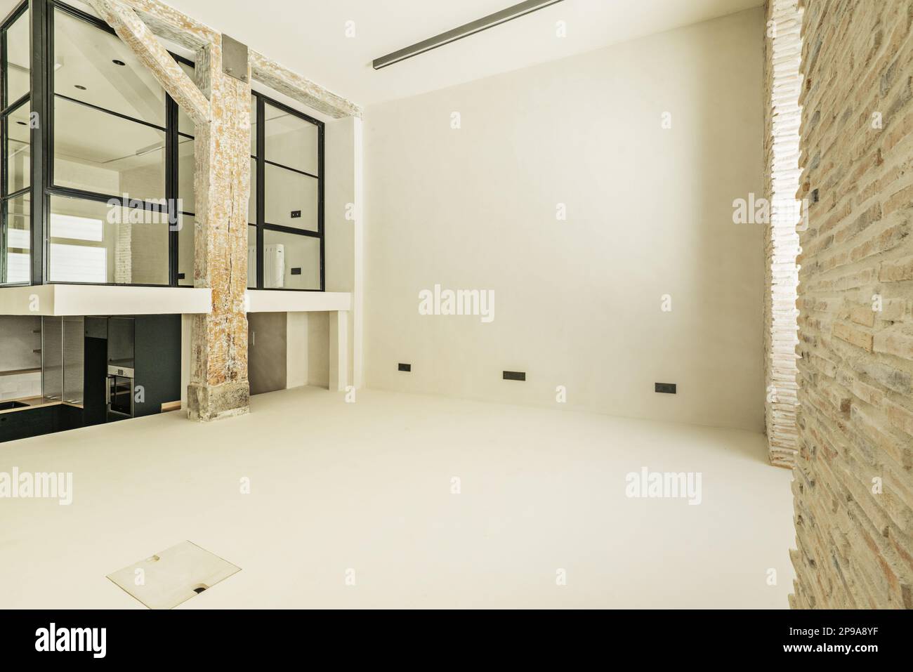 Spazioso loft vuoto con recinzione in metallo e vetro, pavimenti in cemento bianco lucido e pareti di un loft con vecchie colonne e travi in legno Foto Stock