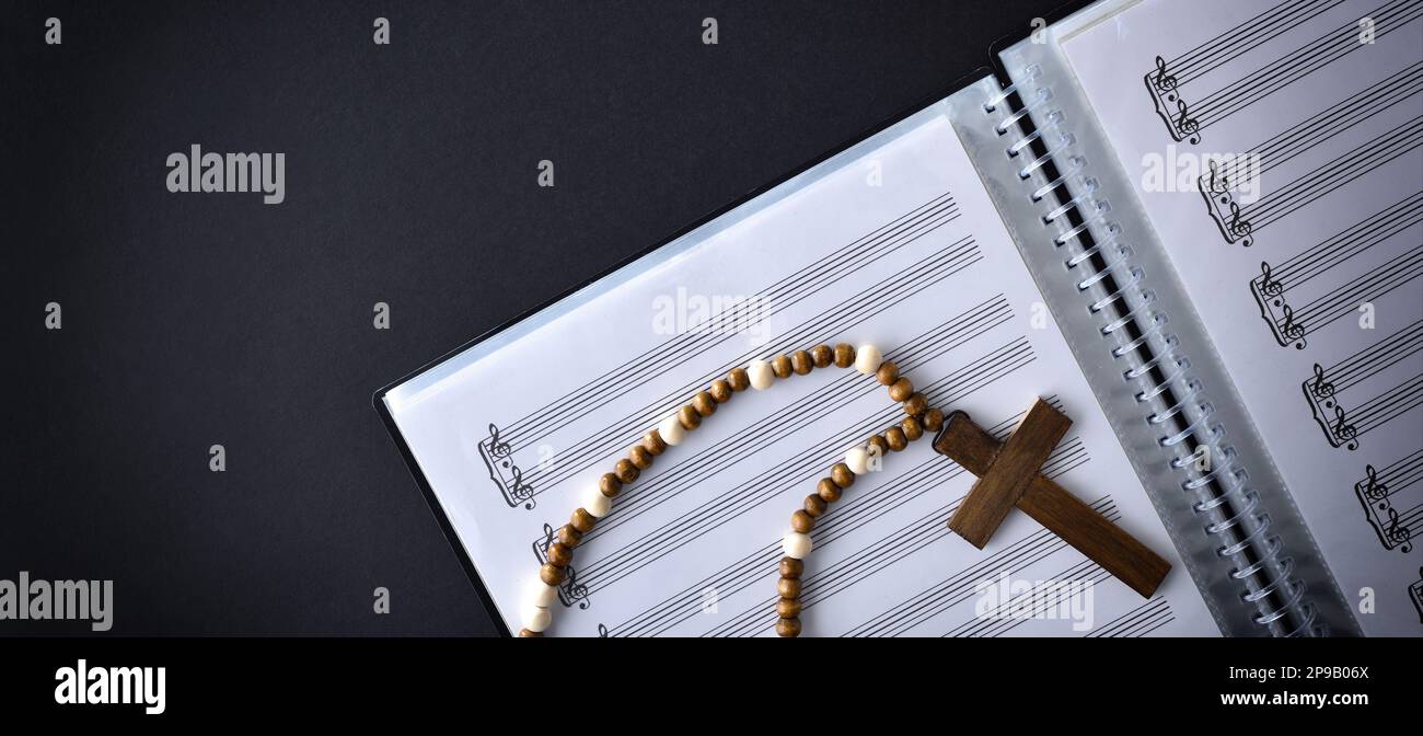 Musica e coro religioso con cartella con spartiti e croce di legno sulla parte superiore del tavolo nero. Vista dall'alto. Foto Stock