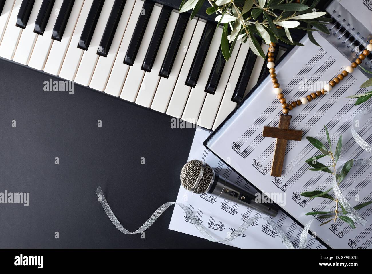 Musica religiosa con pianoforte e cori su un tavolo nero decorato con rami di ulivo e una croce cristiana per le festività della Domenica delle Palme. Vista dall'alto. Foto Stock