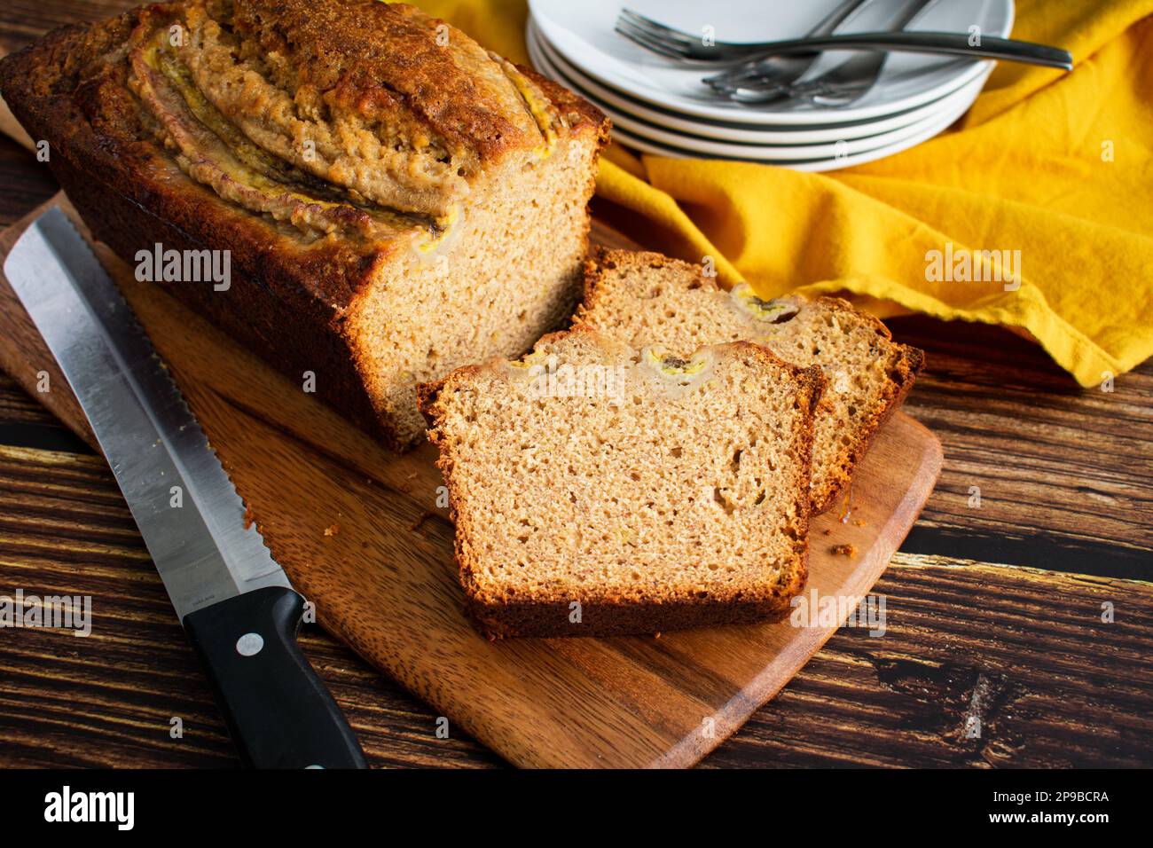 Pane Banana a fette su un tagliere di legno: Fette di pane appena fatto con piatti e forchette sullo sfondo Foto Stock