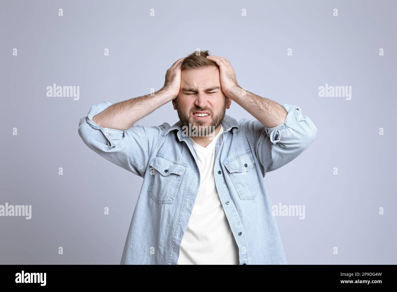 Giovane uomo che soffre di mal di testa su sfondo chiaro Foto Stock