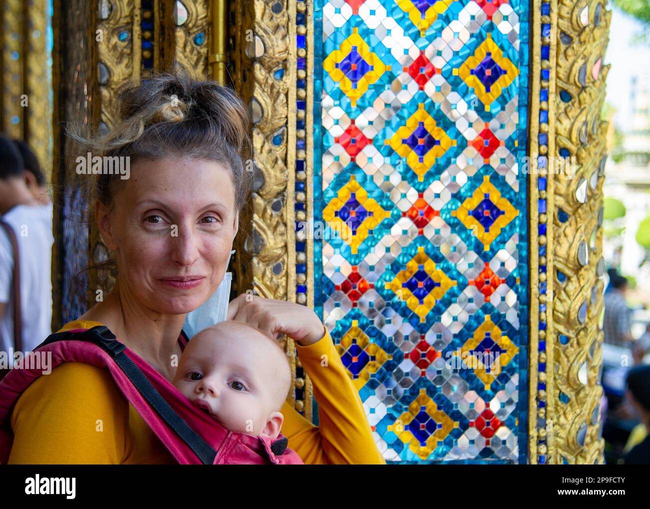 Turista a Bangkok posa con il suo bambino accanto al dettaglio di uno dei chedi dorati al tempio di Wat Phra Kaew in Thailandia Foto Stock