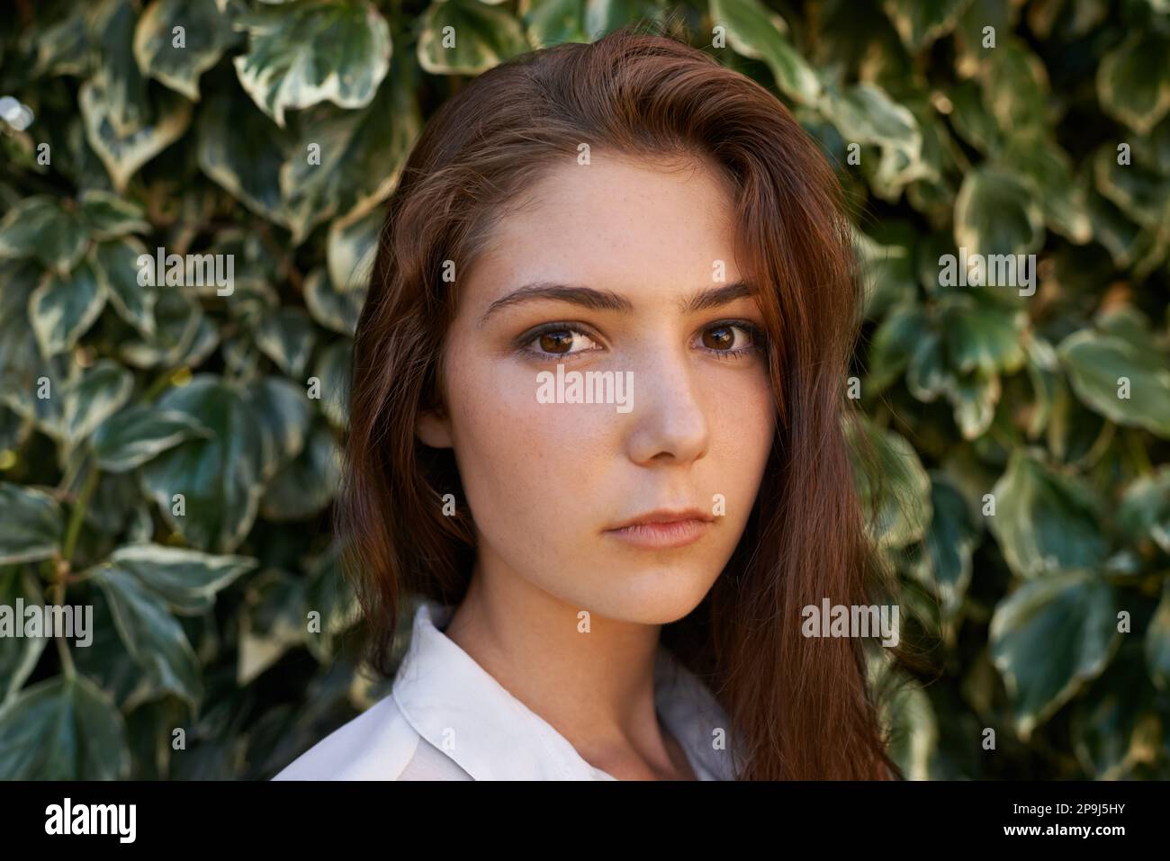 Naturalmente stupendo. Ritratto corto di una giovane donna attraente in piedi davanti ad una grande siepe. Foto Stock