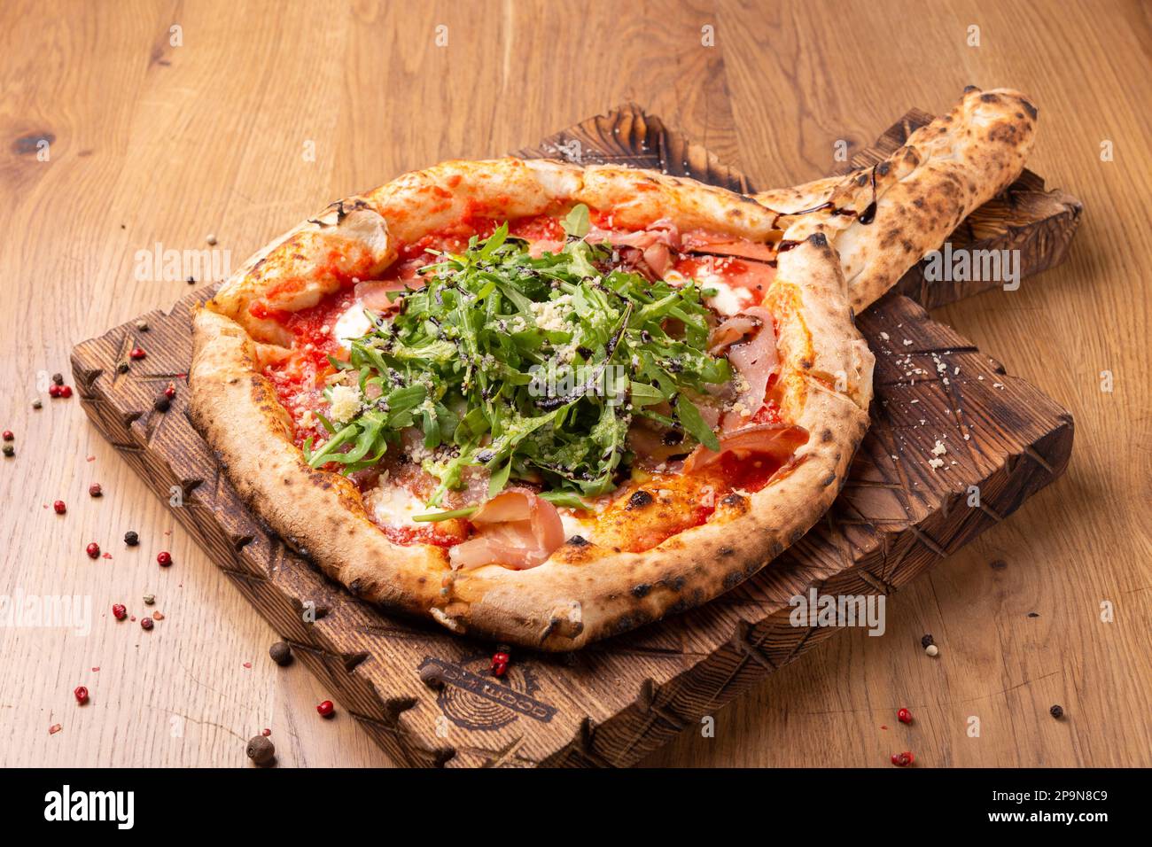 Pizza al forno con mozzarella, prosciutto secco, pomodori, aceto balsamico e rucola su fondo ligneo. Vista ravvicinata Foto Stock