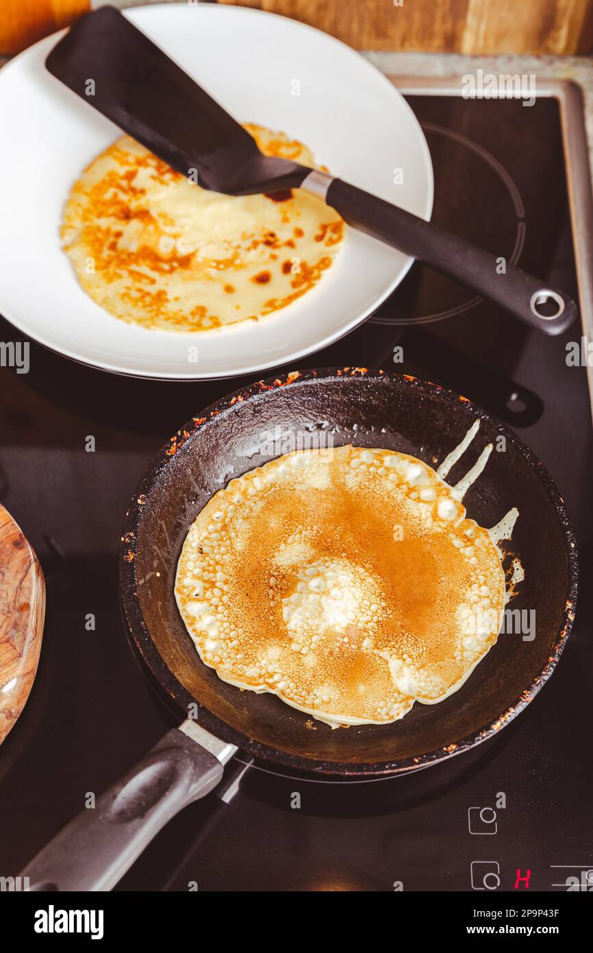 Preparazione di frittelle sottili in padella in cucina, con pasta da cucina per crepes e frittelle. Foto Stock