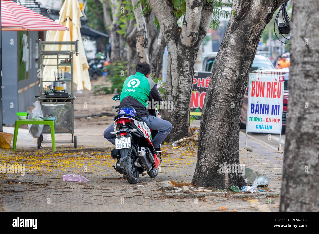 Un motociclista Grab che si riposa sulla sua bicicletta parcheggiata su un marciapiede a ho Chi Minh City, Vietnam. Foto Stock