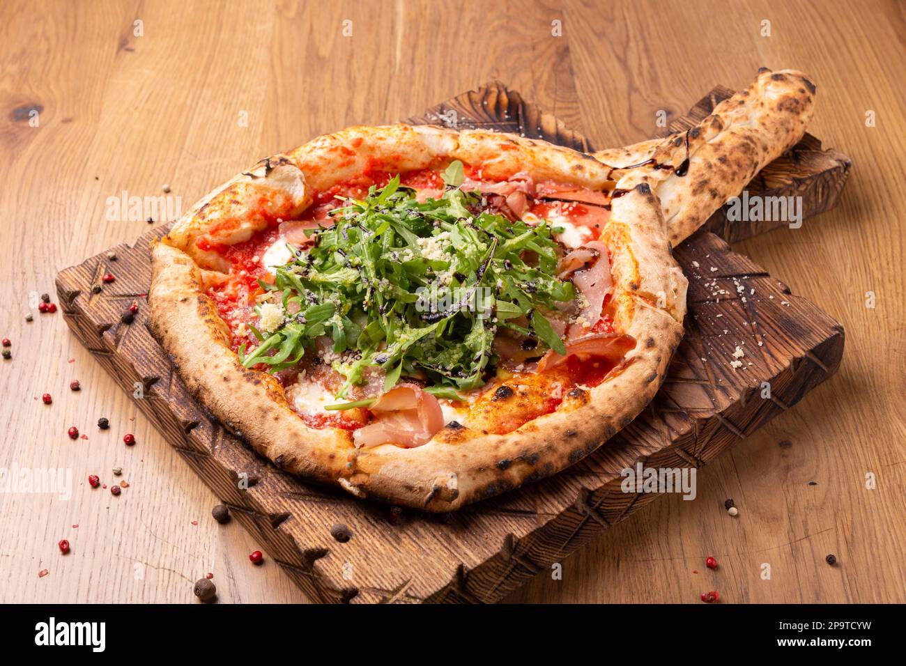 Pizza al forno con mozzarella, prosciutto secco, pomodori, aceto balsamico e rucola su fondo ligneo. Vista ravvicinata Foto Stock