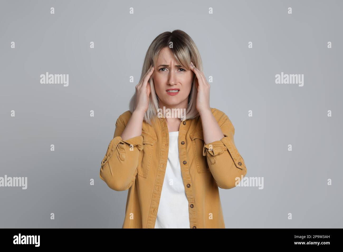 Donna che soffre di mal di testa su sfondo grigio chiaro Foto Stock