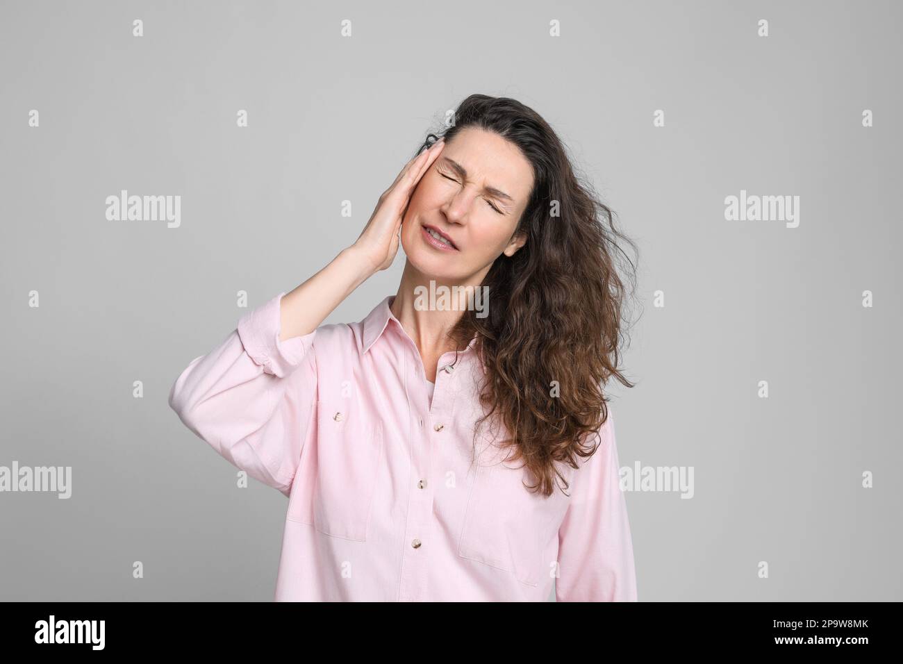 Donna matura che soffre di mal di testa su sfondo grigio chiaro Foto Stock
