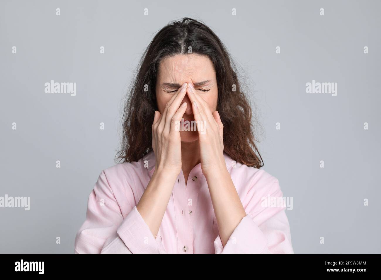 Donna matura che soffre di mal di testa su sfondo grigio chiaro Foto Stock