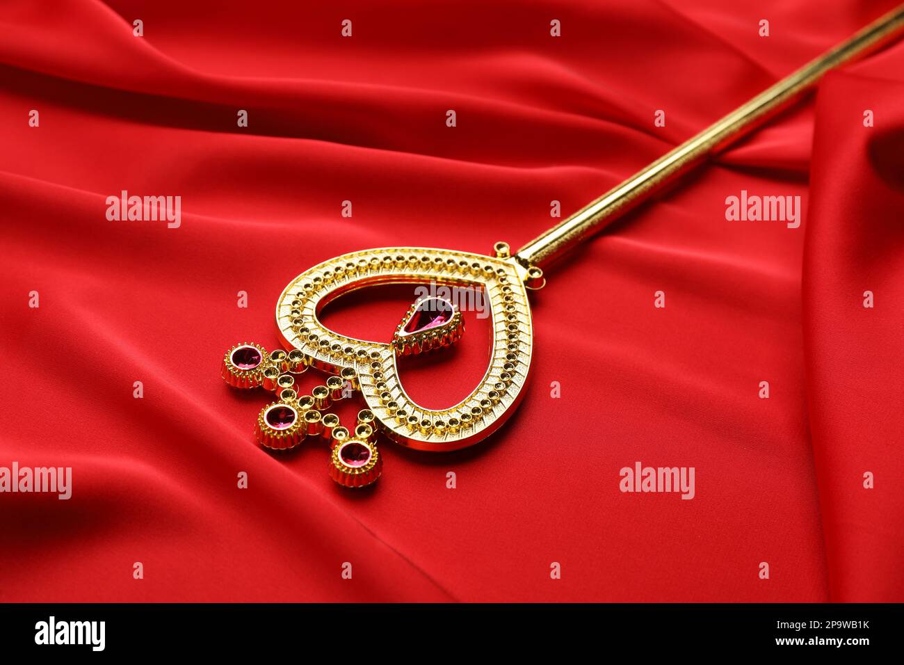 Bella bacchetta magica dorata su tessuto rosso, primo piano Foto Stock
