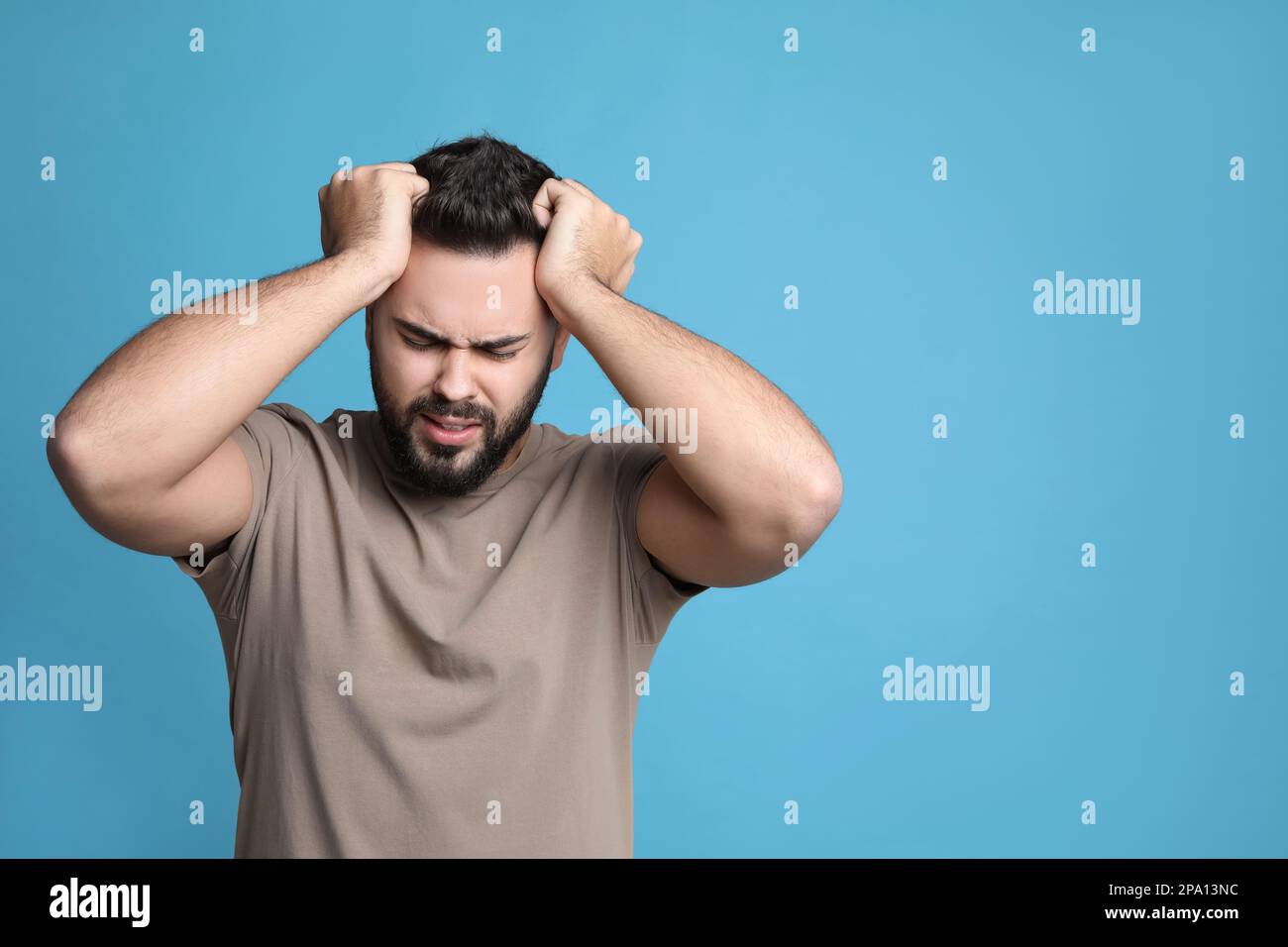 Giovane uomo che soffre di mal di testa su sfondo azzurro, spazio per il testo Foto Stock