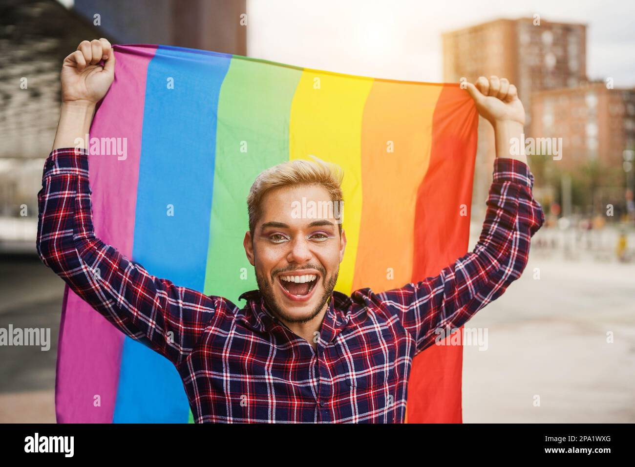 Felice uomo gay che indossa il trucco tenendo lgbt arcobaleno bandiera all'aperto - Focus on face Foto Stock
