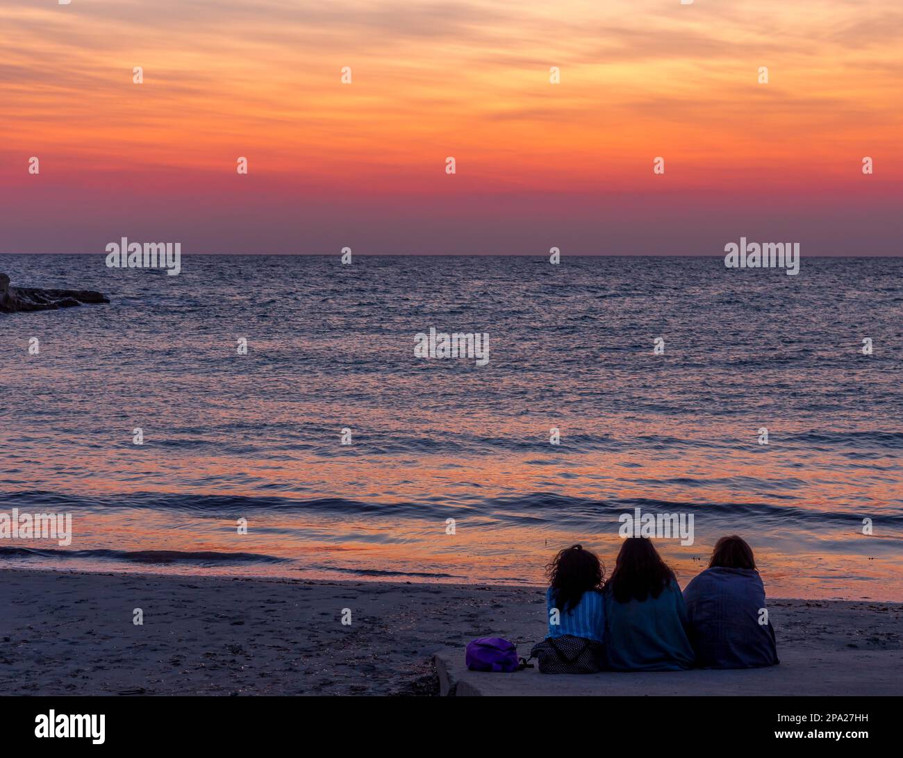 Tre donne in attesa dell'alba di fronte al mare (Puglia) (Sud Italia). Concetto di amicizia, viaggio e avventura Foto Stock